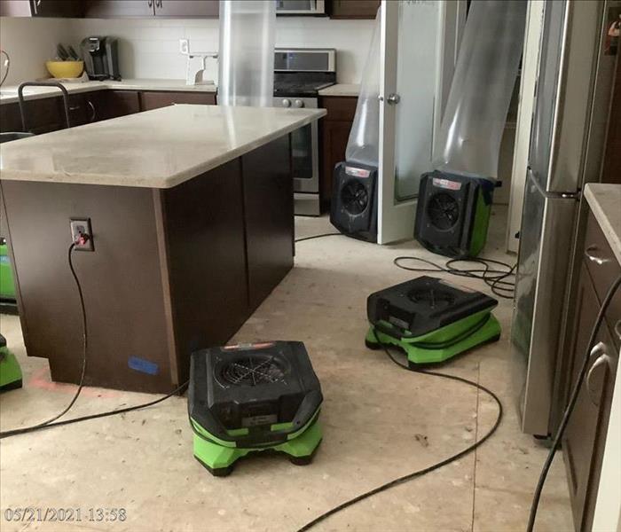 Five SERVPRO air movers and one LGR dehumidifier are positioned around an island counter with plastic sheeting forcing some a