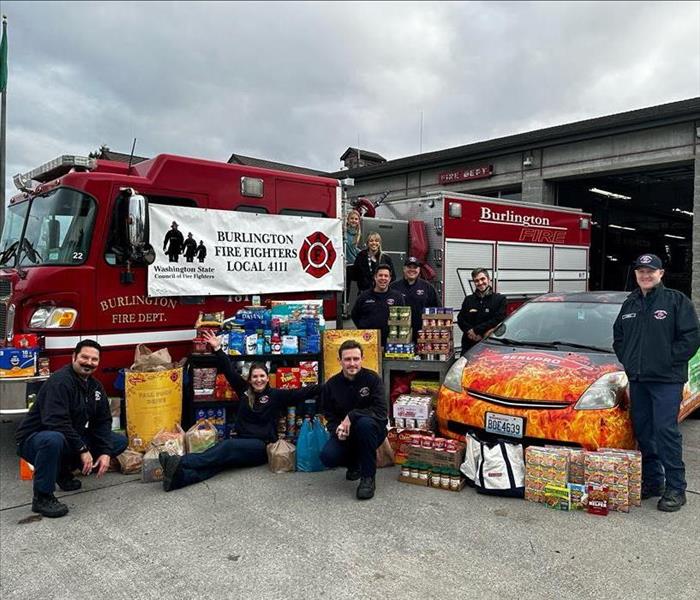 firefighters standing with food from a food drive by their fire truck and a SERVPRO® car