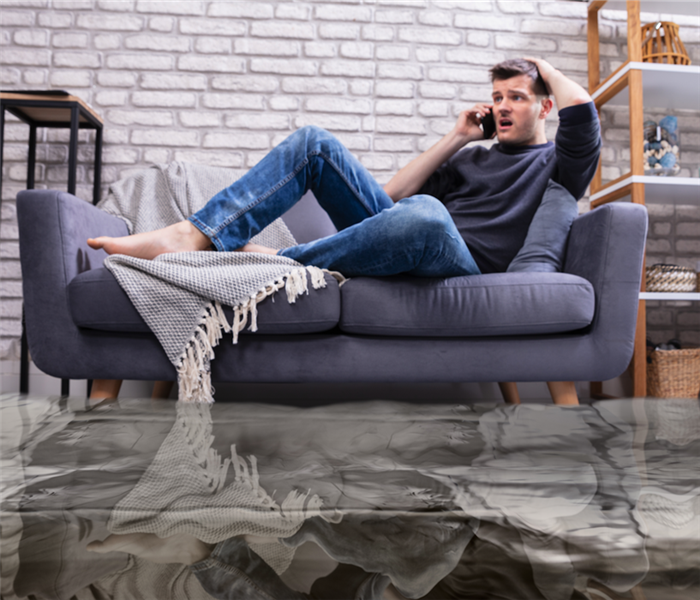 guy sitting on couch in middle of water damaged living room